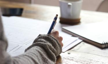 Person with a pen at a desk with papers and an open notebook